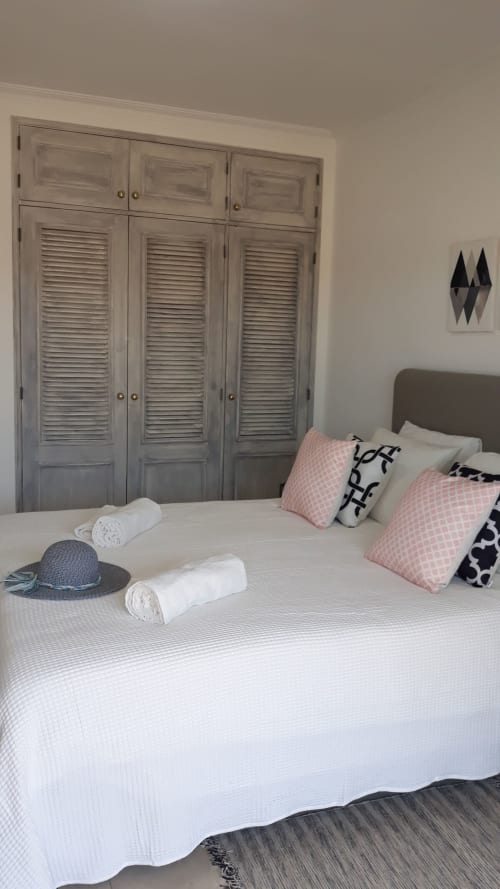 Quarto da cobertura Maresia com cama branca, almofadas rosa, guarda-roupa com venezianas e decoração moderna no Algarve Beach Holidays