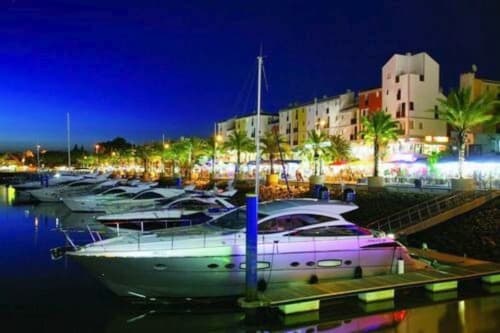 Apartamento Maresia à noite: marina iluminada com iates de luxo, palmeiras e edifícios à beira-mar no Algarve