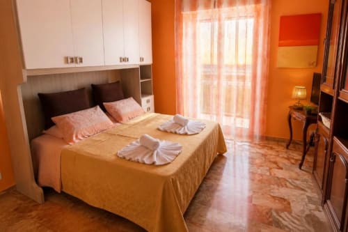Camera luminosa all'Appartamento La Fenice di Varigotti, con copriletto dorato, cuscini bianchi, pareti arancioni e vista sulla città