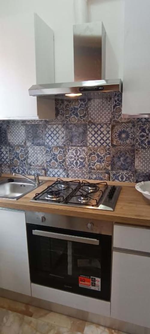 Cucina moderna dell'Apartment La Fenice con piano cottura a gas, forno, piastrelle con motivi decorativi, cappa acciaio inox e