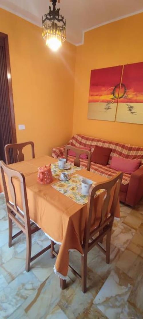 Sala da pranzo giallo brillante con tavolo in legno, divano rosso con cuscini e opera d'arte al tramonto presso L'Appartamento La Fenice