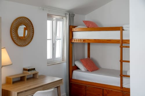 Bright hostel room at Lisbon Poets Inn with wooden bunk bed, red pillows, desk with lamp, and oval mirror on white walls