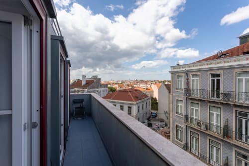 Shared balcony view of Lisbon cityscape from Lisbon Poets Inn hostel, featuring red-roofed buildings and blue sky