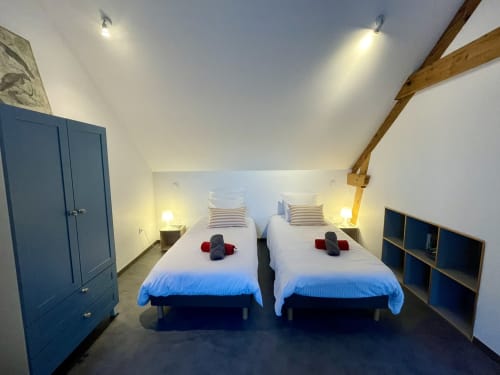 Twin beds in modern cottage bedroom at Les Prairies du Val d'Amboise, Noizay with wooden beams and blue storage.