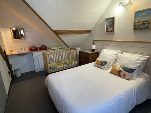 Cozy attic bedroom at Les Prairies du Val d'Amboise with queen bed, wooden crib, and Tours posters in Noizay
