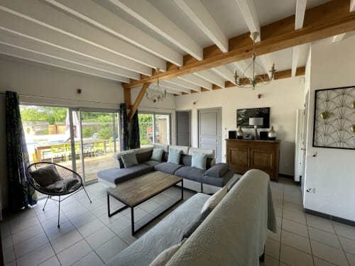 Modern cottage living room with exposed beams, dark sofa, fireplace, and garden access at Les Prairies du Val d'Amboise
