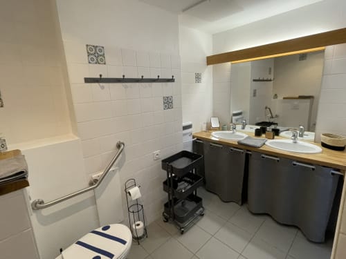 Modern bathroom with dual vanity sinks, white tile walls, black storage cart, and toilet at Les Prairies du Val d'Amboise