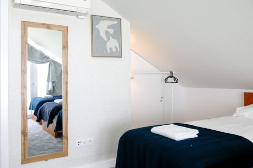Modern bedroom at Lisbon Poets Inn hostel with dark blue bed, wooden-framed mirror, white walls, and minimalist décor