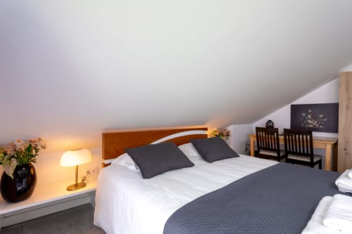 Modern king size bedroom at Lisbon Poets Inn with wooden headboard, dark pillows, bedside lamp, and sloped ceiling