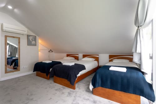 Spacious multi-bed room at Lisbon Poets Inn hostel with three wooden beds, white linens, dark blue bedspreads, and sloped