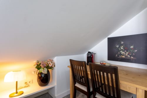Lisbon Poets Inn king bedroom with angled ceiling, desk, black chairs, flowers, and artwork on dark accent wall