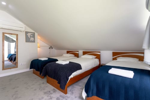 Spacious bedroom at Lisbon Poets Inn with three wooden beds, white bedding, navy throws, and sloped ceiling in this Lisboa