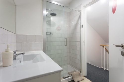 Modern bathroom with white vanity sink and glass-enclosed shower stall at Lisbon Poets Inn hostel in Lisboa