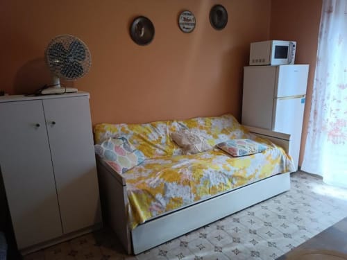 Accogliente monolocale a Residenza Adalgisa con divano letto a fiori gialli, frigorifero bianco, ventilatore e orologi su pareti in cotto.