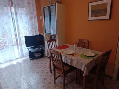 Zona pranzo dell'appartamento Residenza Adalgisa a Finale Ligure, con tavolo apparecchiato, sedie in legno, TV e pareti arancioni