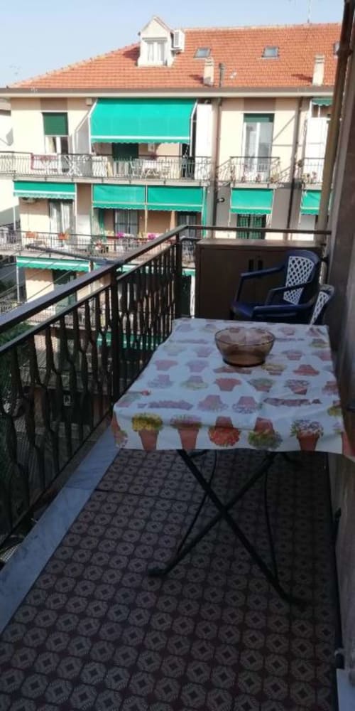 Balcone della Residenza Adalgisa a Finale Ligure con tavolo, sedia e vista sulla città con edifici colorati e tende azzurre
