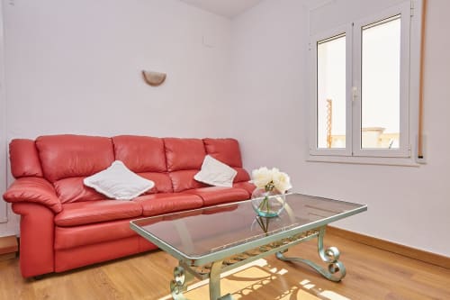 Luminoso salón en Experiencias Encant B&B de Calafat con sofá de cuero rojo, mesa de cristal y paredes blancas