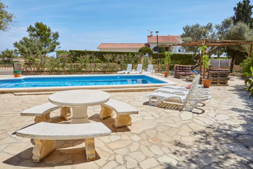 Área de piscina en Experiencias Encant B&B en Calafat con mesas de piedra, tumbonas y jardín mediterráneo