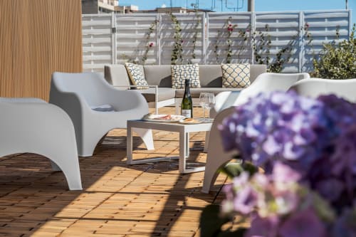 Terrazza moderna sulla tetto di Bluemoon Sardegna a Cagliari con lettini bianchi, divano, ponte in legno e fiori viola