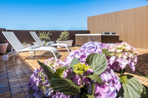 Fiori viola sulla terrazza con solarium di Bluemoon Sardinia, lettini e ponte in legno a Cagliari