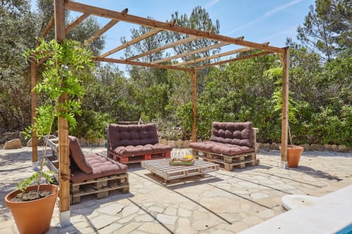 Pérgola de madera con muebles de palets y cojines en un patio rústico de Experiencias Encant, Calafat