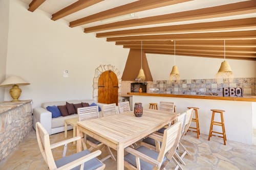 Zona de comedor y cocina de concepto abierto en Experiencias Encant en Calafat con vigas de madera, mesa de comedor y parrilla BBQ.