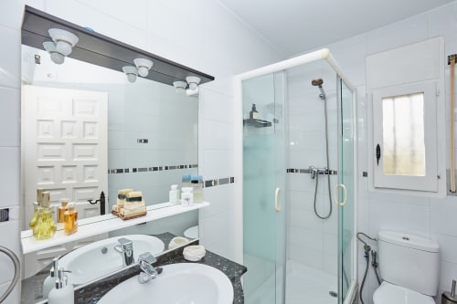 Baño moderno en Experiencias Encant B&B en Calafat con azulejos blancos, ducha de cristal, doble lavamanos y espejo de tocador