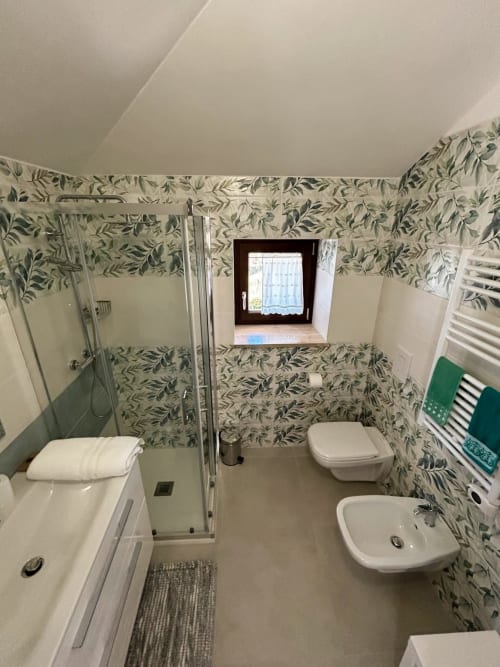 Bagno moderno nella camera Scilla di AgriBio Villa Ribes con carta da parati a motivi floreali, doccia, toilet, bidet e lavabo