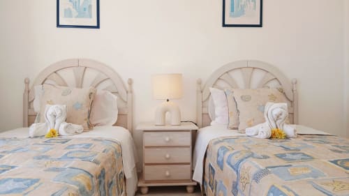 Duas camas de solteiro com colchas estampadas em apartamento em Portimão, cabeceiras bege e criado-mudo compartilhado com luminária
