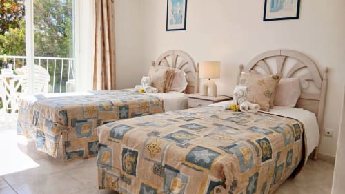 Duas camas individuais com colchas estampadas em quarto claro em Portimão com acesso à varanda e vistas para o mar