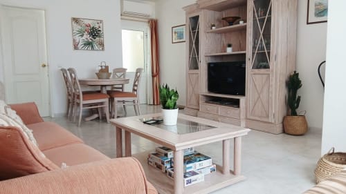 Sala de estar iluminada do apartamento Sweet Home Oasis Parque em Portimão com sofá coral, rack de madeira, mesa de jantar e design moderno