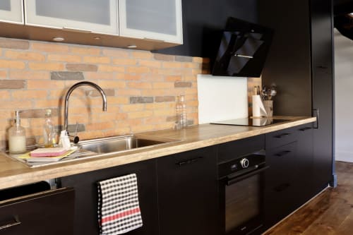 Modern black kitchen in La Maison d'Augustin loft with brick backsplash, wooden countertops, and stainless steel sink
