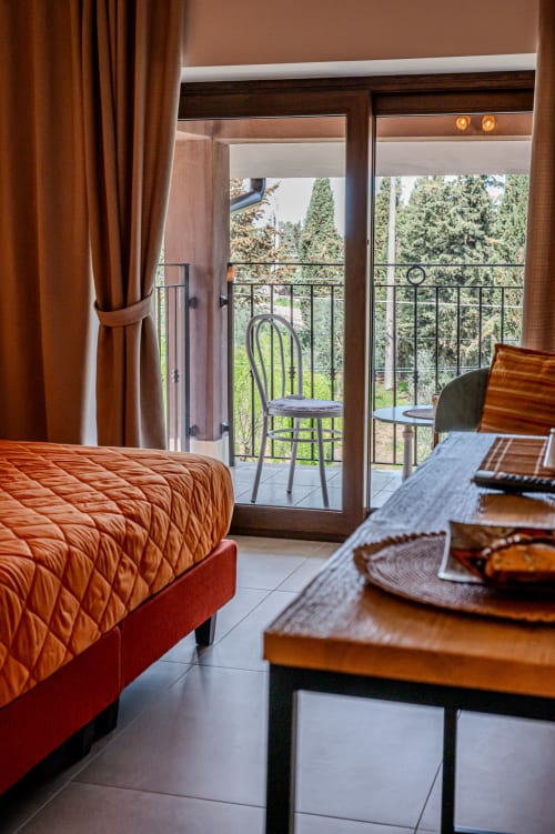 Accogliente camera da letto a AgriBio Villa Ribes con letto trapuntato arancione, balcone con vista sul giardino, porte e mobili in legno scuro
