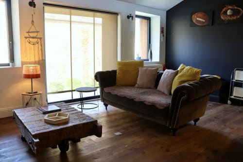 Spacious loft living room at La Maison d'Augustin with dark sofa, wooden coffee table, and garden view from large windows in
