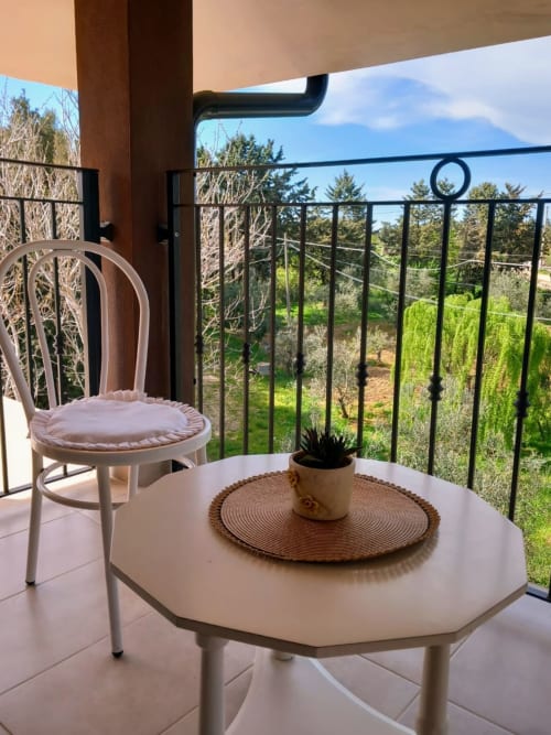 Zona salotto in balcone presso AgriBio Villa Ribes con vista sul giardino, Altamura. Sedia bianca e tavolo con pianta in vaso che si affaccia