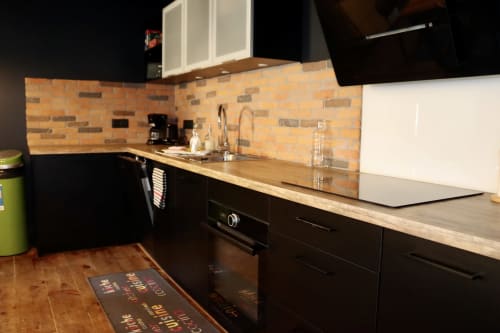 Modern kitchen in La Maison d'Augustin loft, Mont-de-Marsan, with black cabinetry, brick backsplash, and wooden countertop