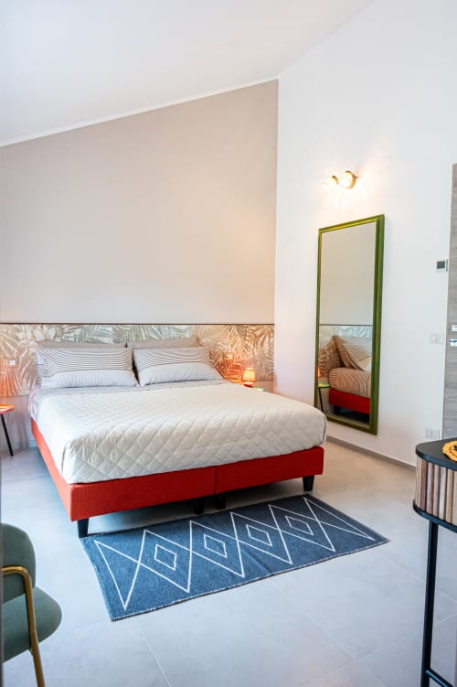 Camera moderna di AgriBio Villa Ribes ad Altamura con letto rosso, cuscini a righe e specchio con cornice verde