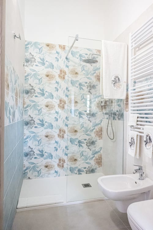 Bagno moderno nella suite Clematide di AgriBio Villa Ribes con doccia rivestita di piastrelle floreali, lavandino bianco e vista sul giardino