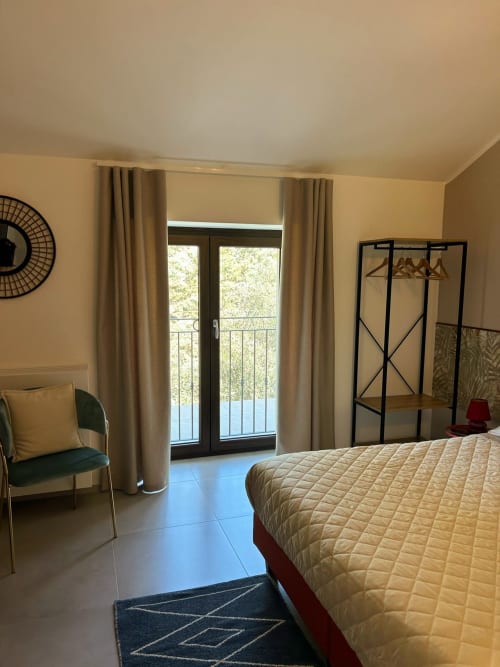 Camera Clematide presso AgriBio Villa Ribes ad Altamura con vista giardino, letto, poltrona e accesso al balcone
