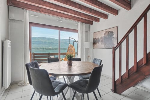 Modern dining room with round table, dark chairs, wooden beams, and expansive lake views at Emmlea, Tresserve