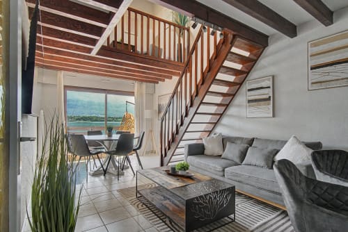 Modern apartment living room with lake view balcony, wooden staircase, gray sofa, and dining area at Emmlea hotel, Tresserve