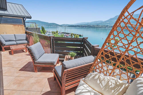 Lakeside balcony at Emmlea hotel in Tresserve with wooden furniture, lake views, and sailboats below.