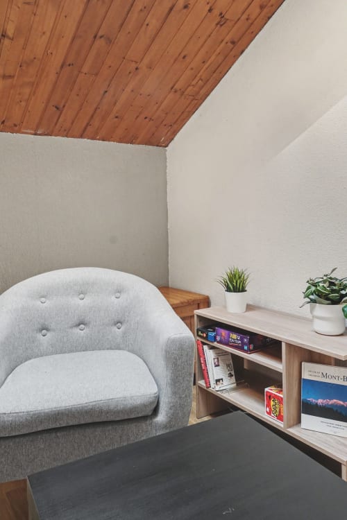 Cozy corner in Le Lac Suspendu apartment at Emmlea with gray armchair, wooden ceiling, potted plants, and shelving unit at