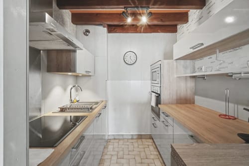 Modern galley kitchen at Emmlea hotel in Tresserve with white cabinets, wooden beams, and natural light