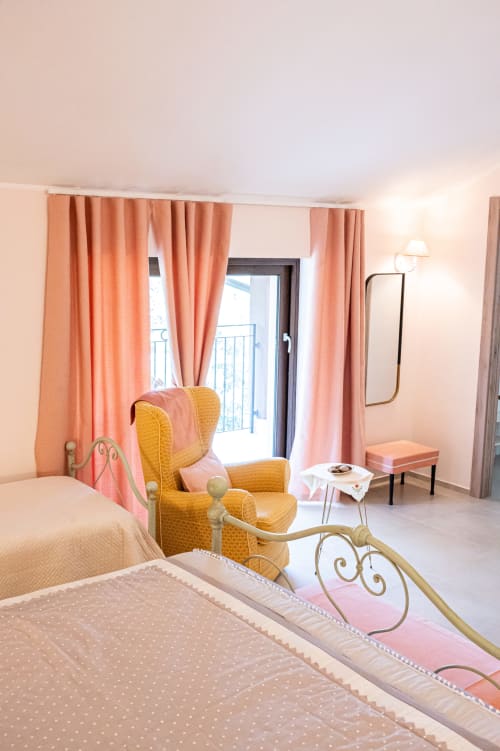 Stanza Orchidea di AgriBio Villa Ribes con poltrona dorata, tende rosa e balcone con vista giardino ad Altamura