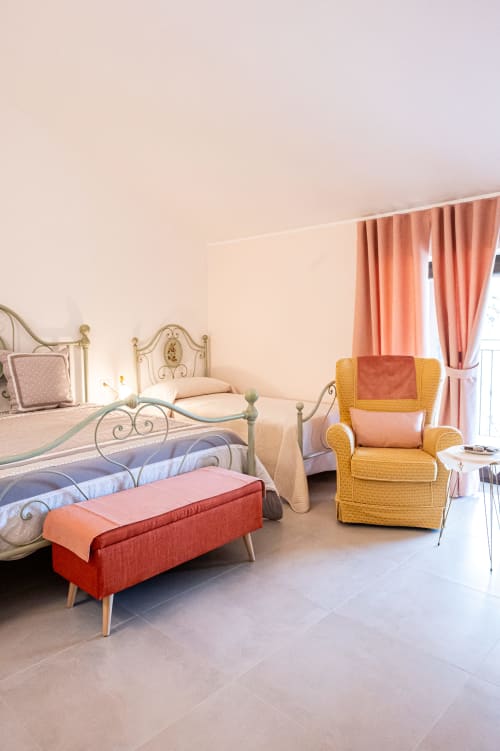 Camera Orchidea di AgriBio Villa Ribes ad Altamura con elegante letto, poltrona gialla e tende con vista sul giardino