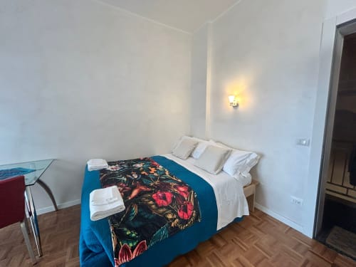 Bedroom at Villa Marisa, Pavia with queen bed, blue floral blanket, white linens, wall sconce, and wooden floor.
