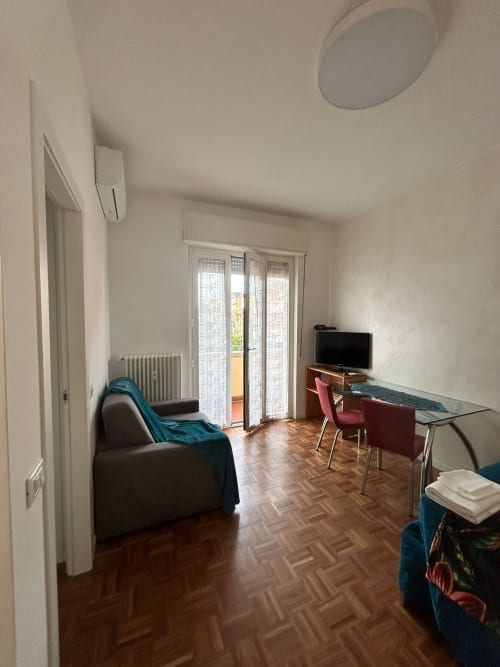 Modern studio apartment at Villa Marisa, Pavia with living area, desk, TV, armchair, glass dining table and garden view doors