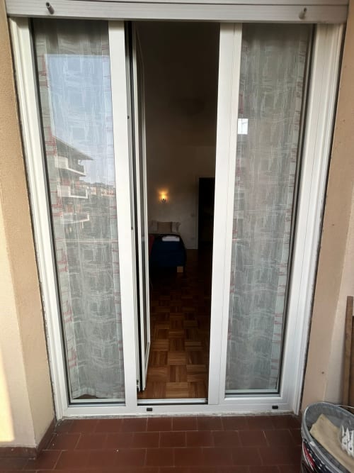 Sliding glass doors opening to furnished apartment at Villa Marisa, Pavia, with wooden floor and sheer curtains
