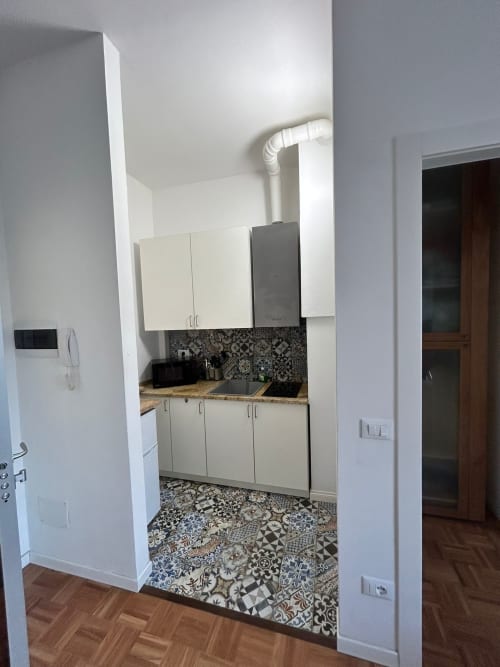 Modern kitchenette in Villa Marisa apartment, Pavia, with white cabinets, black sink, patterned tile floor and backsplash